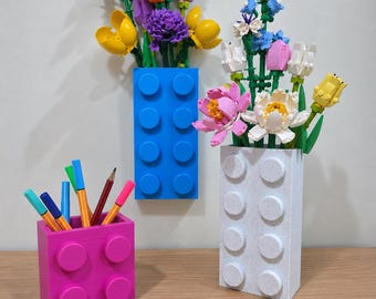 Peut inclure: Un récipient rectangulaire bleu vif et un récipient rectangulaire blanc moucheté, tous deux dotés de tenons circulaires, contenant chacun un bouquet de fleurs en plastique colorées. Un petit récipient carré rose à tenons contient des stylos.