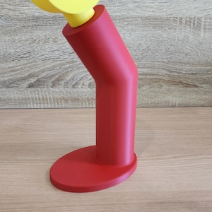 May include: A red and yellow plastic stand with a curved top. The stand is designed to hold a phone or other device.
