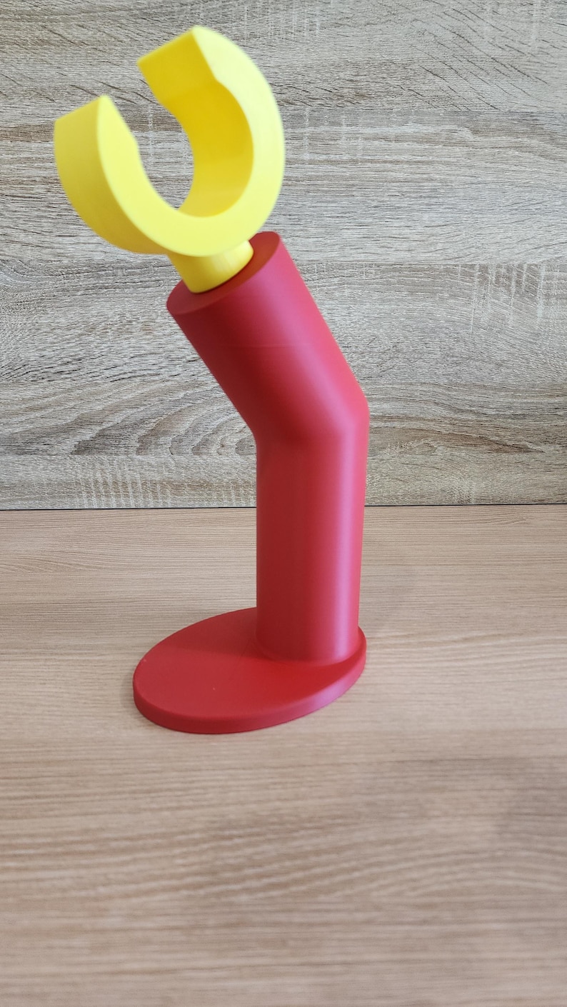 May include: A red and yellow plastic stand with a curved top. The stand is designed to hold a phone or other device.