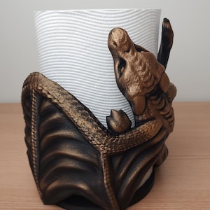 May include: A gold-colored dragon-shaped paper towel holder. The dragon is curled around the paper towel roll and has a detailed, textured design.