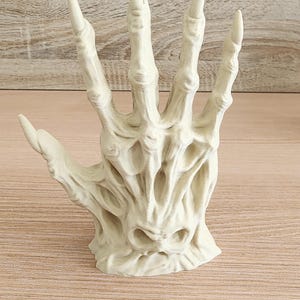 Peut inclure: Sculpture en r&eacute;sine blanc cass&eacute; repr&eacute;sentant une main squelettique ouverte. Les doigts sont longs et pointus, avec des d&eacute;tails osseux et une texture marqu&eacute;e. L'aspect vieilli sugg&egrave;re un objet ancien ou d'&eacute;poque. Id&eacute;al pour une d&eacute;coration d'Halloween.