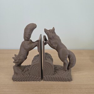 Op de afbeelding: Bruine wolf boekensteunen. Elke boekensteun toont een wolf die naar een centraal paneel springt. De basis van de boekensteunen heeft een boomstam- en grasontwerp. De boekensteunen zijn gemaakt van een stevig materiaal.