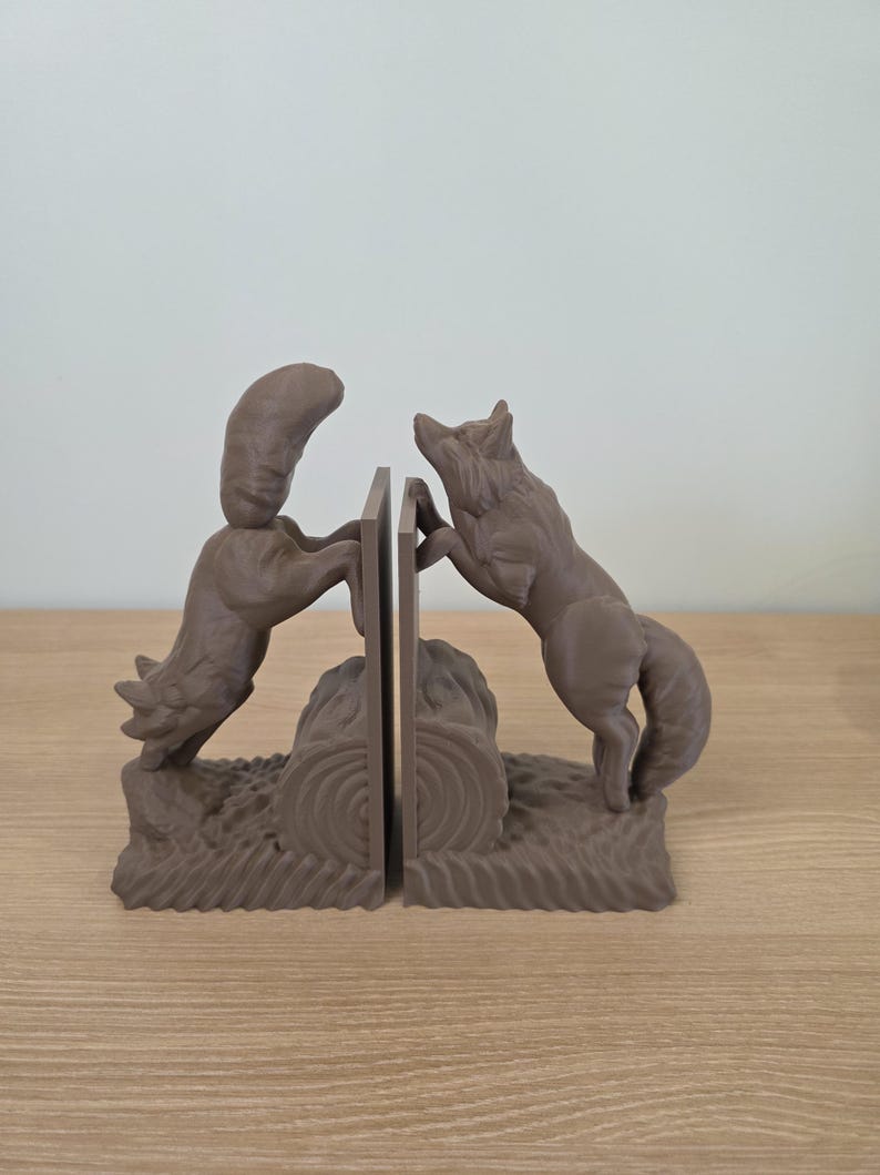 Op de afbeelding: Bruine wolf boekensteunen. Elke boekensteun toont een wolf die naar een centraal paneel springt. De basis van de boekensteunen heeft een boomstam- en grasontwerp. De boekensteunen zijn gemaakt van een stevig materiaal.