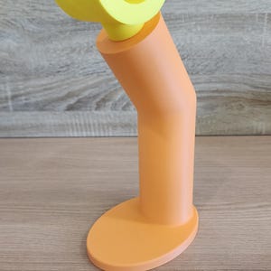 May include: A yellow and orange plastic phone stand with a curved top and a round base.
