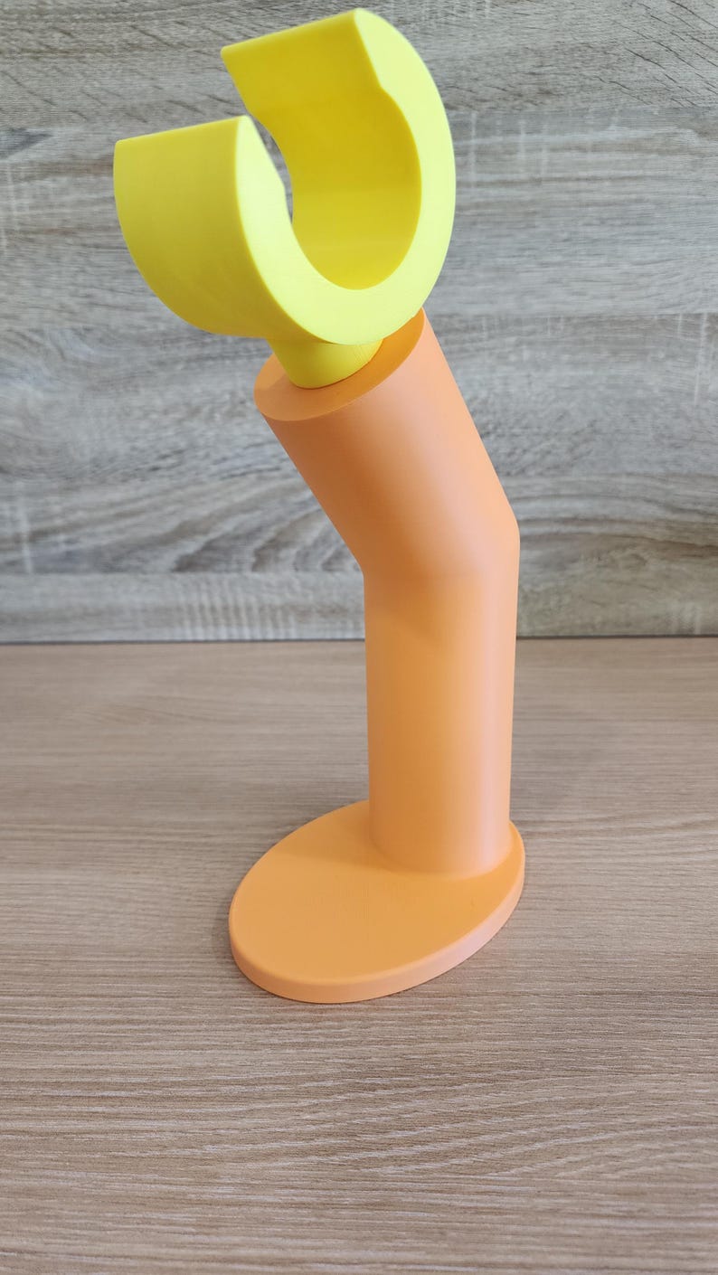 May include: A yellow and orange plastic phone stand with a curved top and a round base.