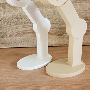 May include: Two 3D printed articulated arms, one white and one beige, with a rounded base. The arms are designed to resemble a robotic arm.