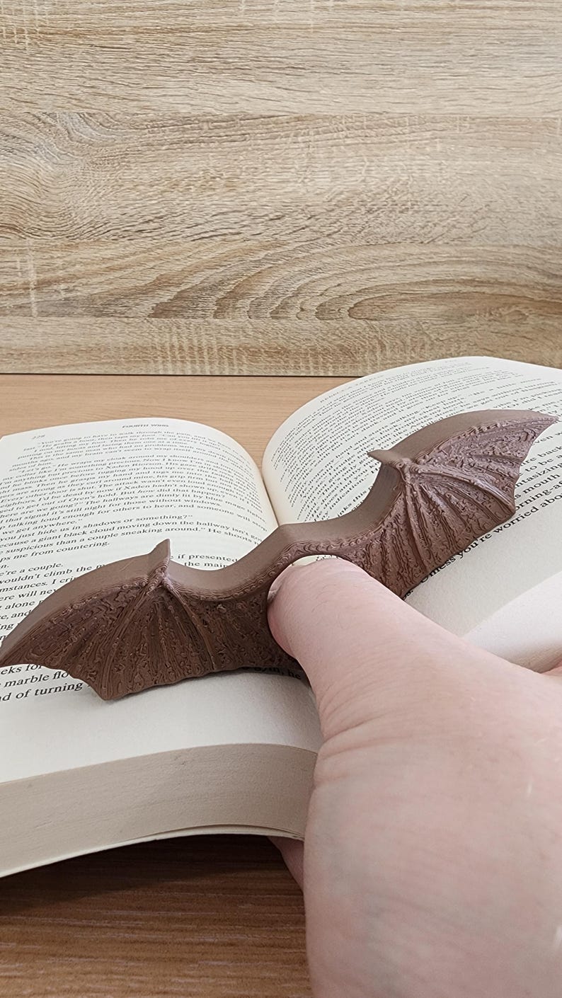 May include: A brown, dragon-shaped book holder with wings spread open, holding a book open. The book holder is made of a textured material and has a realistic design.