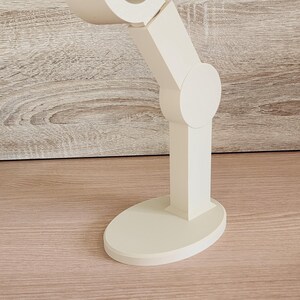 May include: A white plastic stand with a curved arm, designed to hold a phone or other device.