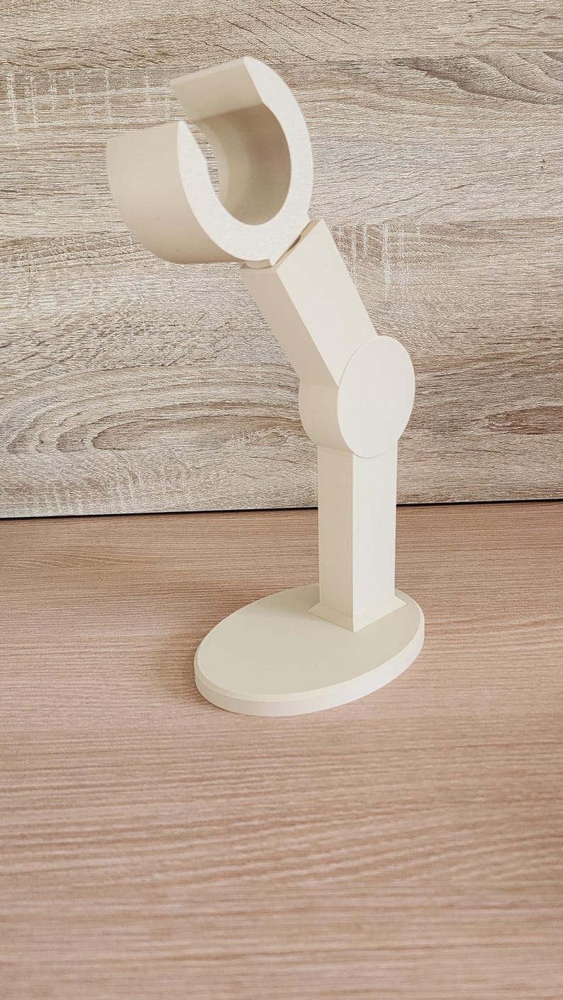 May include: A white plastic stand with a curved arm, designed to hold a phone or other device.