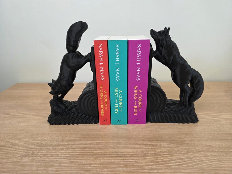 Op de afbeelding: Zwarte wolf-boekensteunen met drie boeken. De boeken heten "A Court of Thorns and Roses", "A Court of Mist and Fury" en "A Court of Wings and Ruin" van Sarah J. Maas. De boekensteunen staan op een houten oppervlak.