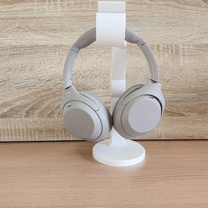 May include: A pair of beige over-ear headphones are displayed on a white stand. The headphones have a sleek, modern design.