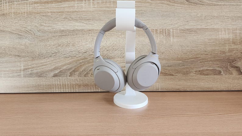 May include: A pair of beige over-ear headphones are displayed on a white stand. The headphones have a sleek, modern design.