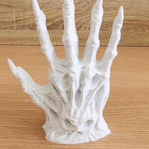 Peut inclure: Sculpture d'une main ouverte et d&eacute;taill&eacute;e, avec une finition blanche tachet&eacute;e et textur&eacute;e. Les doigts sont longs et pointus, et le design g&eacute;n&eacute;ral a une esth&eacute;tique squelettique et gothique. C'est un objet d&eacute;coratif.