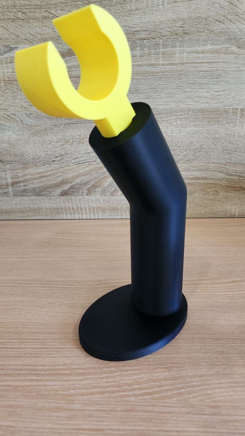 May include: A black and yellow 3D printed phone stand with a curved arm and a round base.