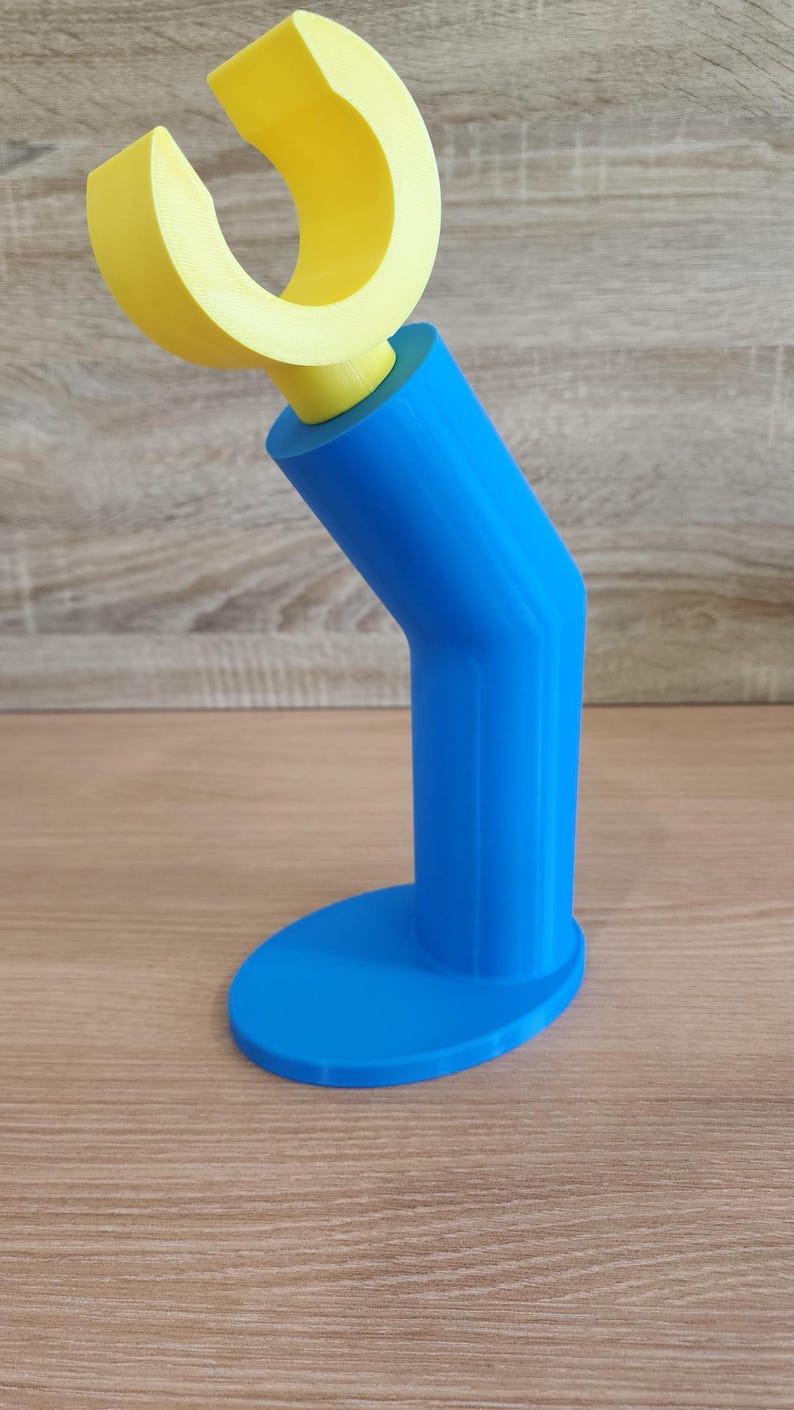 May include: A blue and yellow 3D printed phone stand with a curved top for holding a phone.