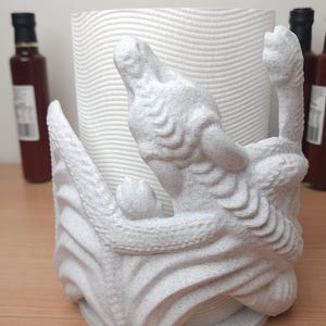 May include: White ceramic paper towel holder shaped like a dragon with a textured surface.