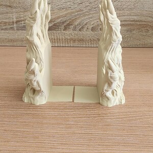 Peut inclure: Paire de serre-livres sculpt&eacute;s blanc cass&eacute; avec un design textur&eacute; et organique. Les serre-livres ont une apparence stylis&eacute;e en forme de flamme et sont pos&eacute;s sur une base beige clair. Le fond est une surface en bois brun clair.