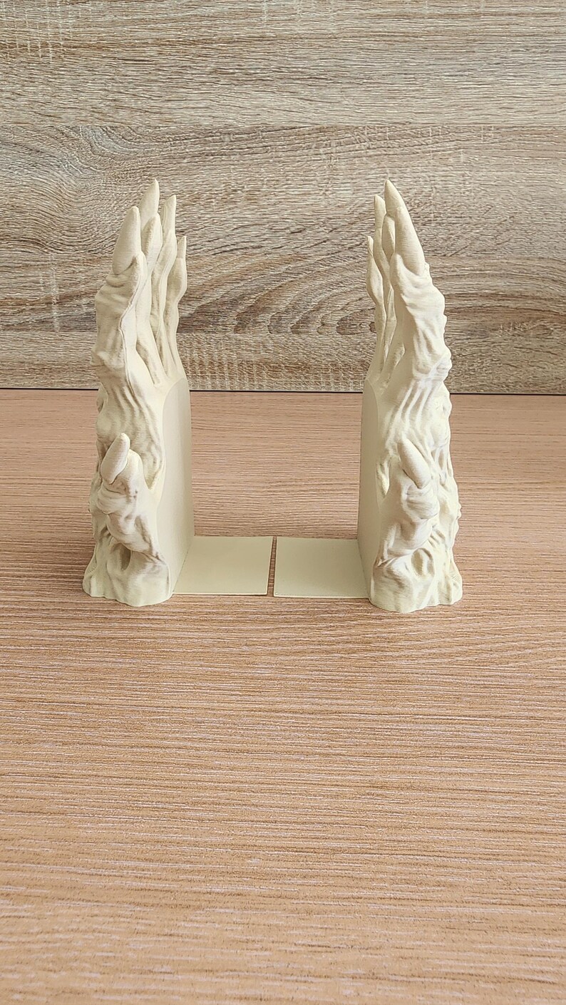 Peut inclure: Paire de serre-livres sculpt&eacute;s blanc cass&eacute; avec un design textur&eacute; et organique. Les serre-livres ont une apparence stylis&eacute;e en forme de flamme et sont pos&eacute;s sur une base beige clair. Le fond est une surface en bois brun clair.