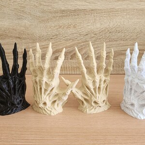 Peut inclure: Ensemble de sculptures de mains d&eacute;coratives en noir, beige et blanc. Les mains ont une apparence squelettique, en forme de griffes, avec de longs doigts pointus. Les sculptures sont dispos&eacute;es sur une surface en bois.