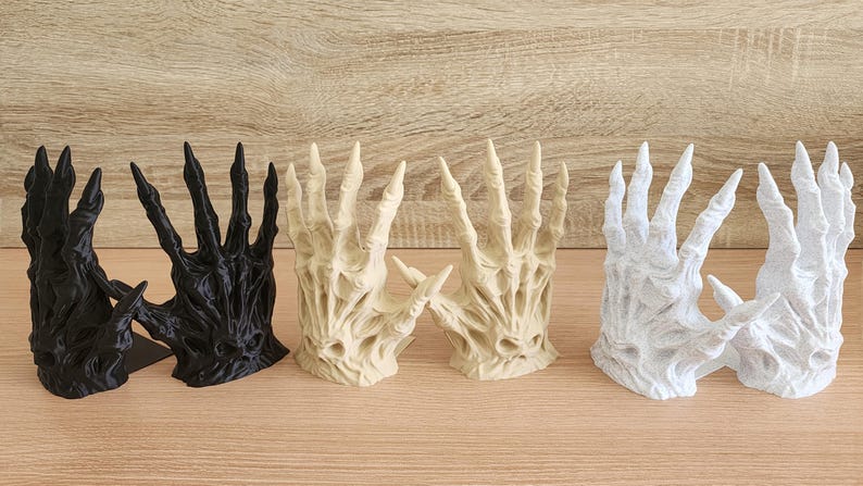 Peut inclure: Ensemble de sculptures de mains d&eacute;coratives en noir, beige et blanc. Les mains ont une apparence squelettique, en forme de griffes, avec de longs doigts pointus. Les sculptures sont dispos&eacute;es sur une surface en bois.
