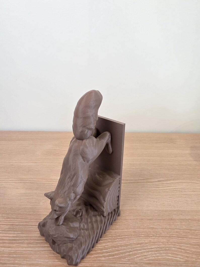 Op de afbeelding: Een bruine vossensculptuur die op een houten constructie klimt. De vos wordt in volle klim gepresenteerd, met zijn voorpoten omhoog. De sculptuur staat op een houten oppervlak.