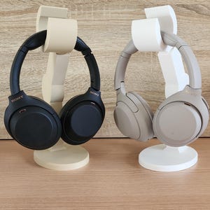 May include: Two pairs of wireless headphones on stands. One pair is black and the other is beige.