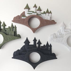 May include: Three bookends shaped like a bridge with a castle on top. The bookends are in three different colors: green, brown, and white.