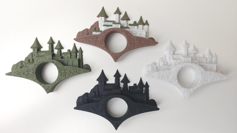 May include: Three bookends shaped like a bridge with a castle on top. The bookends are in three different colors: green, brown, and white.