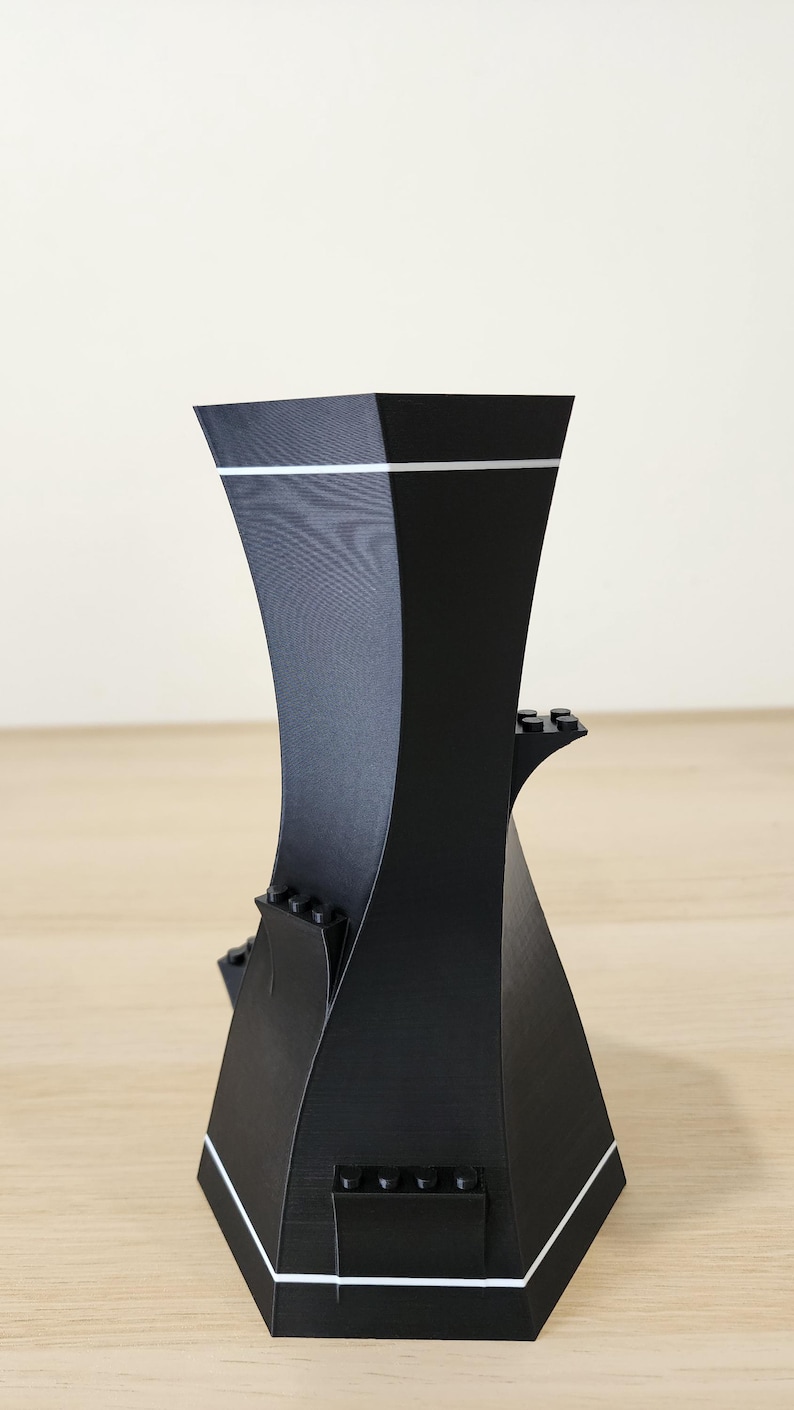May include: Black 3D printed phone stand with a geometric design and white accents. The stand has multiple slots for holding phones and other devices.