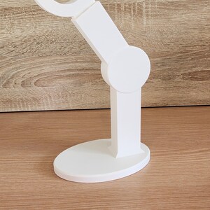 May include: White plastic phone stand with a curved arm and a round base.