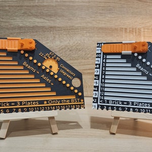 Two brick rulers next to each other. Black and orange on the left and the black and white on the right. There is a Lego flower and Lego pot behind the black and orange ruler on the left.