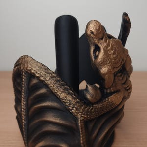 May include: A black and gold dragon-shaped paper towel holder. The dragon is curled up with its wings spread out. The holder is made of a durable material and is perfect for adding a touch of whimsy to any kitchen.