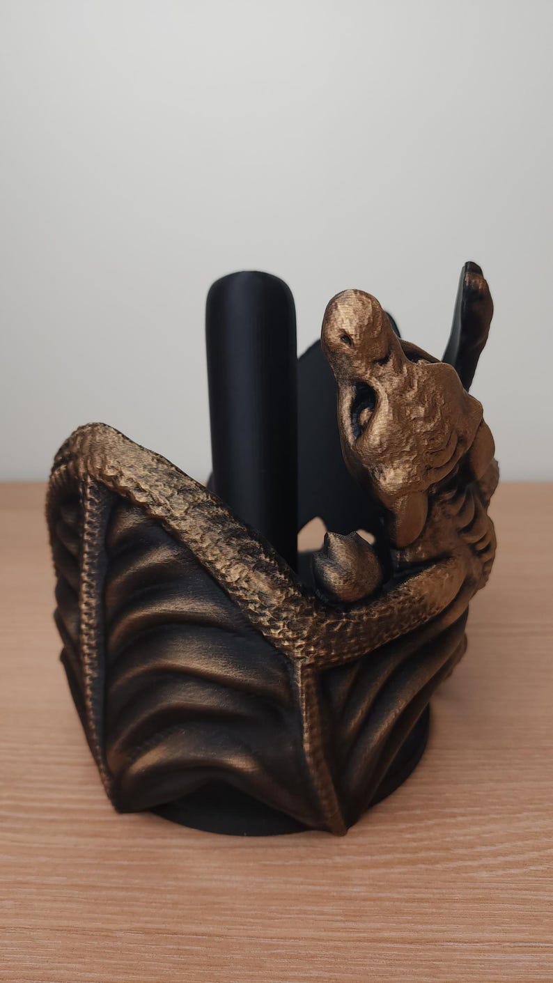 May include: A black and gold dragon-shaped paper towel holder. The dragon is curled up with its wings spread out. The holder is made of a durable material and is perfect for adding a touch of whimsy to any kitchen.