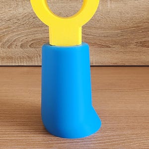 May include: A yellow plastic toy building block with a blue base. The block has a U-shaped opening on top.