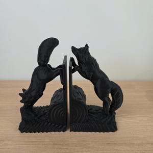 Op de afbeelding: Zwarte wolf boekensteunen. Elke boekensteun heeft een gedetailleerde wolf, de ene springt en de andere staat, die een centrale steun flankeren. De boekensteunen zijn gemaakt van een solide zwart materiaal en zijn ontworpen om boeken rechtop te houden.
