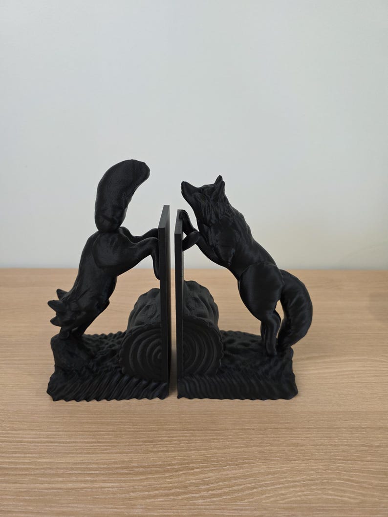 Op de afbeelding: Zwarte wolf boekensteunen. Elke boekensteun heeft een gedetailleerde wolf, de ene springt en de andere staat, die een centrale steun flankeren. De boekensteunen zijn gemaakt van een solide zwart materiaal en zijn ontworpen om boeken rechtop te houden.