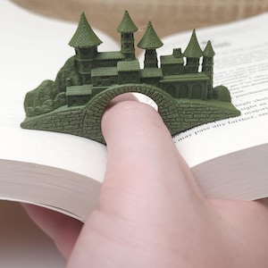 May include: A green 3D printed castle bookmark with a bridge that can hold a finger. The bookmark is designed to hold a page in a book.
