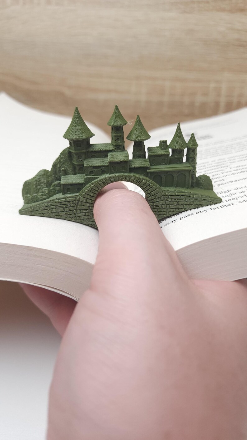 May include: A green 3D printed castle bookmark with a bridge that can hold a finger. The bookmark is designed to hold a page in a book.