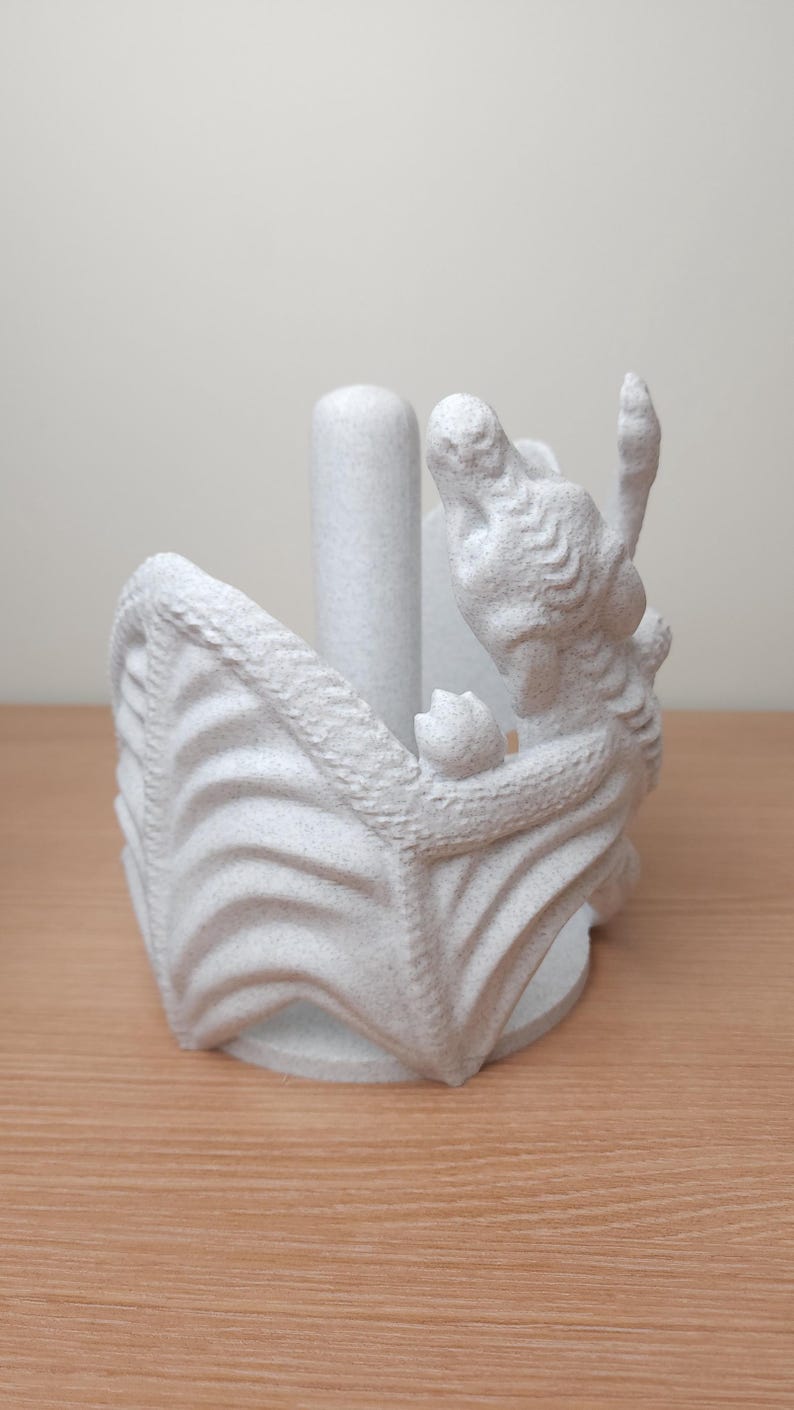 May include: White ceramic dragon paper towel holder. The dragon is curled around a central cylinder, with its wings forming the base of the holder.