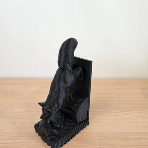 Op de afbeelding: Een zwarte 3D-geprinte boekensteun met een gestileerde wolf die over een boomstam springt. De boekensteun heeft een rechthoekige achterkant en een getextureerde basis, wat een dynamisch en artistiek ontwerp cre&euml;ert.