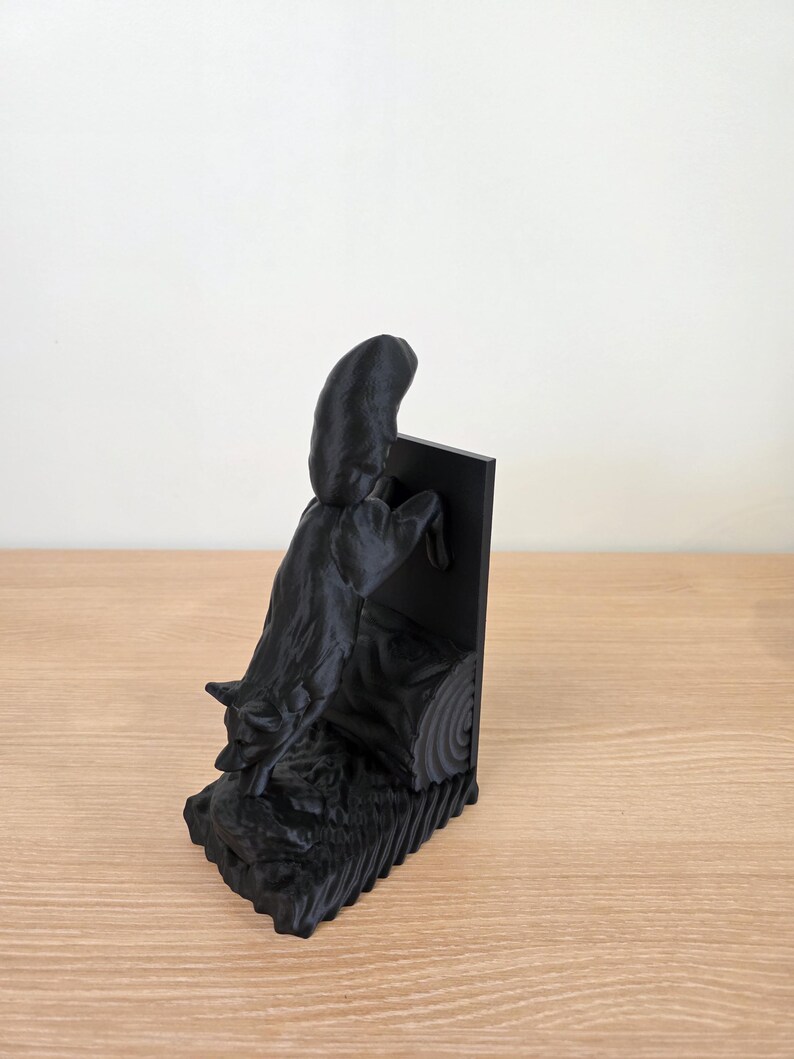 Op de afbeelding: Een zwarte 3D-geprinte boekensteun met een gestileerde wolf die over een boomstam springt. De boekensteun heeft een rechthoekige achterkant en een getextureerde basis, wat een dynamisch en artistiek ontwerp cre&euml;ert.