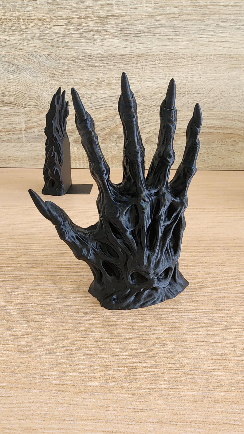 Peut inclure: Sculpture d'une main noire avec de longs doigts pointus. La main est finement d&eacute;taill&eacute;e avec une surface textur&eacute;e et une apparence squelettique. Une deuxi&egrave;me sculpture plus petite est visible en arri&egrave;re-plan.