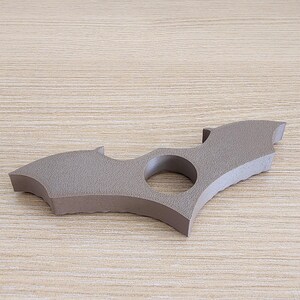 May include: A brown plastic bat-shaped ring with a hole in the center. The ring is textured and has a slightly rough surface.