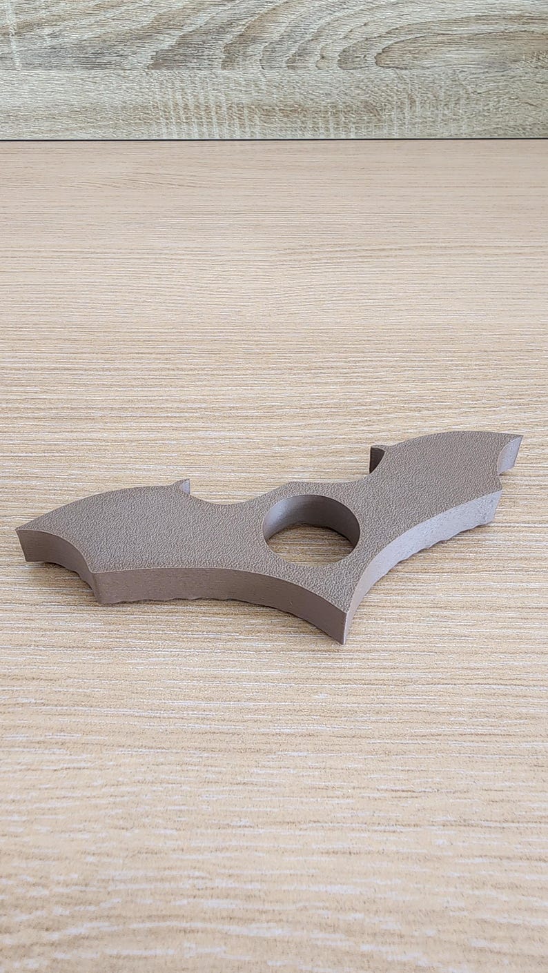 May include: A brown plastic bat-shaped ring with a hole in the center. The ring is textured and has a slightly rough surface.