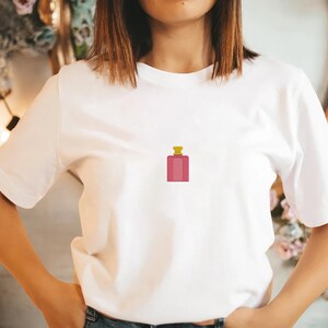 Peut inclure: T-shirt blanc avec un petit motif brod&eacute; d'un flacon de parfum rose et d'un bouchon jaune. Le t-shirt est de style col rond.