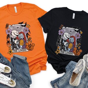 Pu&ograve; includere: Due t-shirt con una stampa grafica di Jack Skellington e Sally di The Nightmare Before Christmas. La grafica &egrave; una carta dei tarocchi con il testo "The Lovers". Una t-shirt &egrave; arancione e l'altra &egrave; nera. Entrambe le t-shirt sono abbinate a jeans e scarpe.