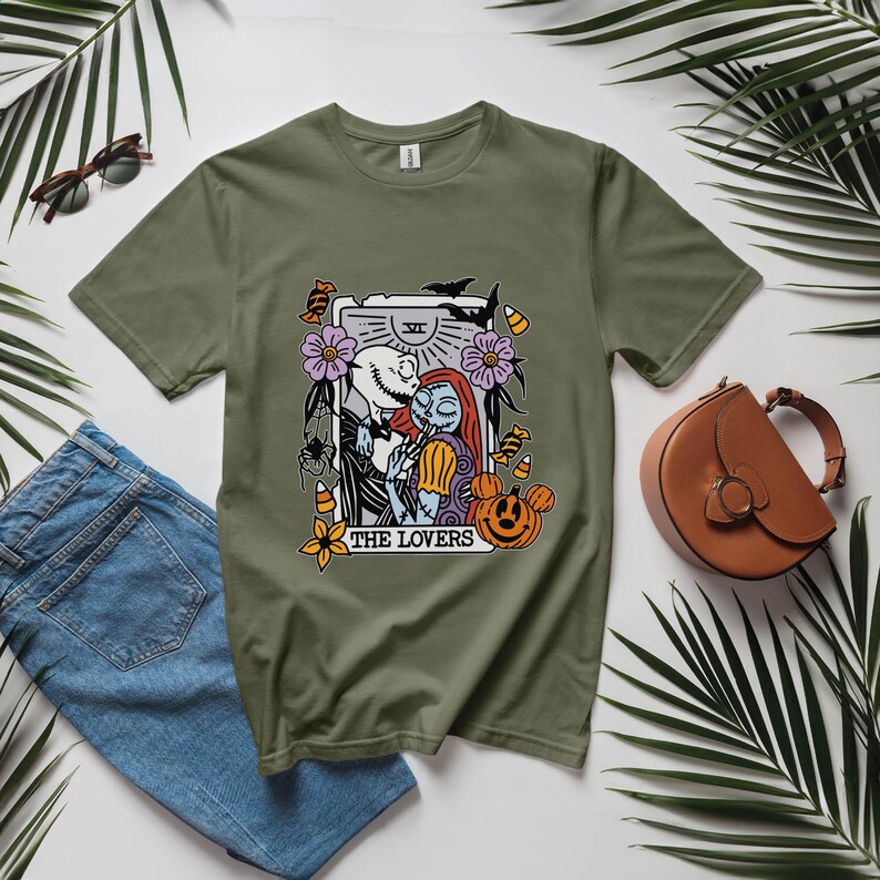 Pu&ograve; includere: Una maglietta verde con una grafica di Jack Skellington e Sally di The Nightmare Before Christmas. La grafica &egrave; una carta dei tarocchi con il testo "The Lovers" e il numero "VI" su di essa.