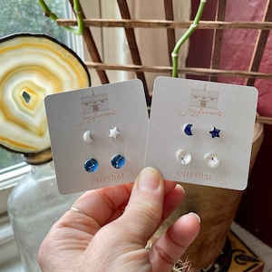 May include: Two sets of celestial-themed earrings on white cards. The cards have the text "joyfivecents" and "CELESTIAL". The earrings are white and blue with moon, star, and constellation designs.