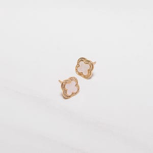 May include: A pair of gold earrings with a white clover design. The clover is surrounded by small clear stones.