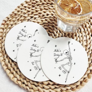 Könnte beinhalten: Weiße Keramikuntersetzer mit einem schwarzen Skelett-Design, Martini-Glas und dem Text "Mike's Dirty 30 Est. 1995". Die Untersetzer liegen auf einem gewebten Platzset, mit einem Glas Wasser und Zitronenscheiben.